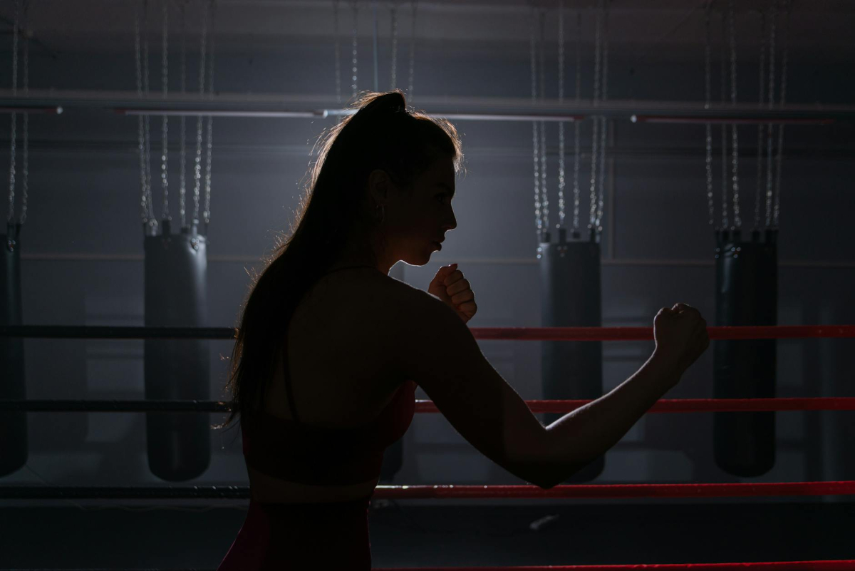 Silhouette of a female boxer in a gym preparing for training. Strong and determined focus highlighting a self-defense mindset.